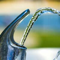 In Rastatt (Baden-Württemberg) startet ein neuartiger Filter zur Entfernung von PFAS aus dem Trinkwasser. Das Projektpilotprojekt zeigt, wie sich Kommunen auf strengere Grenzwerte vorbereiten können und die giftige Ewigkeitschemikalien aus dem Trinkwasser filtern können. In Rastatt filtert eine neue Anlage PFAS aus dem Trinkwasser. Die Stadtwerke Rastatt haben eine kombinierte Enthärtungs- und Aktivkohlefilteranlage in Betrieb genommen, die gesundheitlich bedenkliche per- und polyfluorierte Alkylsubstanzen (PFAS) aus dem Grundwasser entfernt. Hintergrund ist die seit Jahren bekannte Belastung des Grundwassers der Region mit PFAS, die sich in der Umwelt kaum abbauen und mit gesundheitlichen Risiken wie hormonellen Störungen und womöglichen Krebsfolgen in Verbindung gebracht werden. Die Stadtwerke haben rund 8,5 Millionen Euro in den Umbau des Wasserwerks Ottersdorf investiert. Das Land Baden-Württemberg beteiligte sich mit 670.000 Euro an dem Projekt, das bundesweit als Pilotbeispiel für die Anpassung kommunaler Infrastruktur an kommende Grenzwerte gilt. Ab 2026 schreibt die EU für eine Gruppe von PFAS-Verbindungen einen Summengrenzwert von 0,1 Mikrogramm pro Liter im Trinkwasser vor, ab 2028 kommen strengere Einzelstoffgrenzwerte hinzu. Die neue Anlage in Ottersdorf erfüllt diese Anforderungen schon jetzt. Auch das zweite zentrale Wasserwerk in Rastatt, Rauental, wurde bereits mit vier Aktivkohlefiltern ausgestattet, die laut Betreiber rund 2,4 Kilogramm PFAS aus mehr als sechs Millionen Kubikmetern Rohwasser entfernt haben. Die Filtertechnik basiert auf der Adsorption von PFAS-Molekülen an poröser Aktivkohle, die regelmäßig ausgetauscht und wiederaufbereitet wird. In Rauental wird zusätzlich ein Ionenaustauscher im Pilotbetrieb getestet, der vor allem kurzkettige PFAS binden soll. Diese gelten als schwerer zu entfernen, sind aber ebenfalls relevant für die Einhaltung künftiger Grenzwerte. Laut Umweltbundesamt liegt der Aufwand für die PFAS-Entfernung mit Aktivkohle in realen Anlagen derzeit bei unter zehn Cent pro Kubikmeter. Preislich vertretbar, aber mit dauerhaftem Betriebsaufwand verbunden. Der Standort Rastatt gilt bundesweit als besonders belastet: Im Landkreis sind über 160.000 Menschen betroffen, das Grundwasser ist auf über 1.000 Hektar Fläche kontaminiert. Die Stadtwerke Rastatt arbeiten seit über einem Jahrzehnt an Lösungen, haben unter anderem neue Brunnen gebohrt, Monitoringprogramme aufgebaut, wissenschaftliche Pilotprojekte angestoßen und Klagen gegen mutmaßliche Verursacher und öffentliche Stellen eingereicht. Inzwischen gilt das Unternehmen bundesweit als Vorreiter im Umgang mit PFAS im Trinkwasser. Mit dem Start der erweiterten Anlage in Ottersdorf steht nun ein weiterer Baustein der langfristigen Versorgungssicherung. Die Erfahrungen aus Rastatt fließen in Fachdebatten und Gesetzgebungsverfahren auf Landes- und EU-Ebene ein – ein Hinweis darauf, dass die Nachfrage nach solcher Technik künftig auch überregional steigen dürfte. Foto von Daniel Hooper ? auf Unsplash